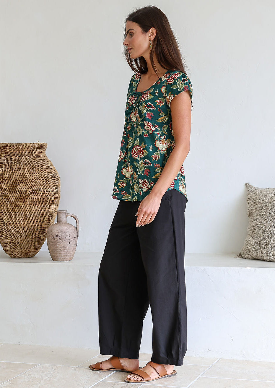 Woman standing sideways wears 100 percent cotton top with short cap sleeves and longer back hem.