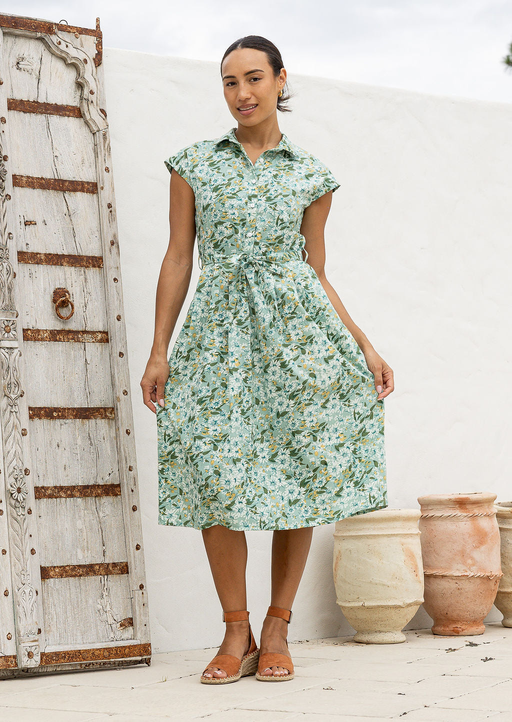 Woman wearing a shirt style cotton midi length dress with buttoned bodice, pockets, collar and cap sleeves