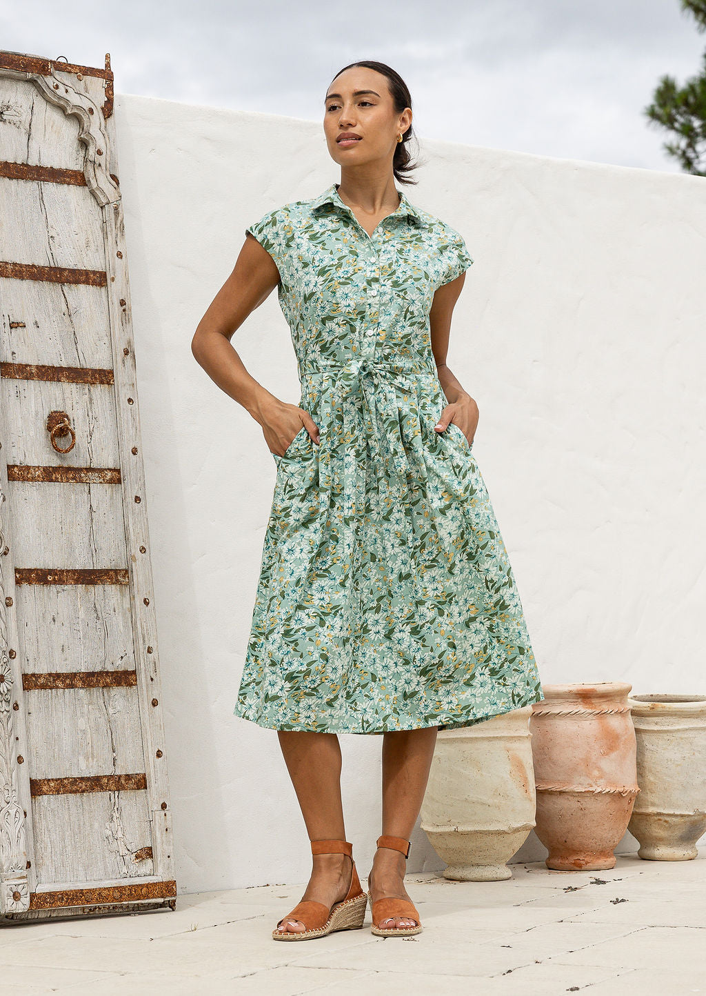 Model posing in a sage green based floral print shirt style 100% cotton dress with cap sleeves and detachable waist tie