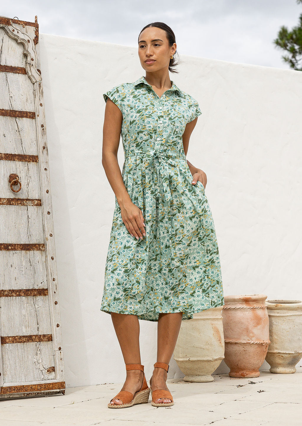 Woman wearing a shirt style cotton midi length dress with buttoned bodice, pockets, collar and cap sleeves