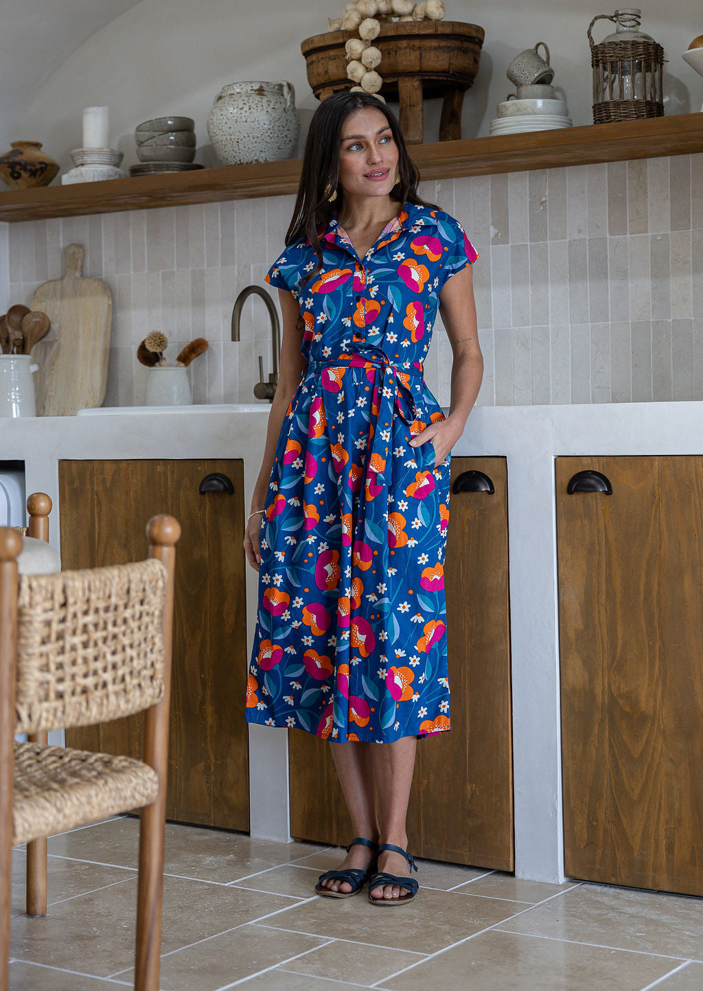 Woman wearing a midi length navy based floral cotton dress with buttoned bodice and one hand in pocket