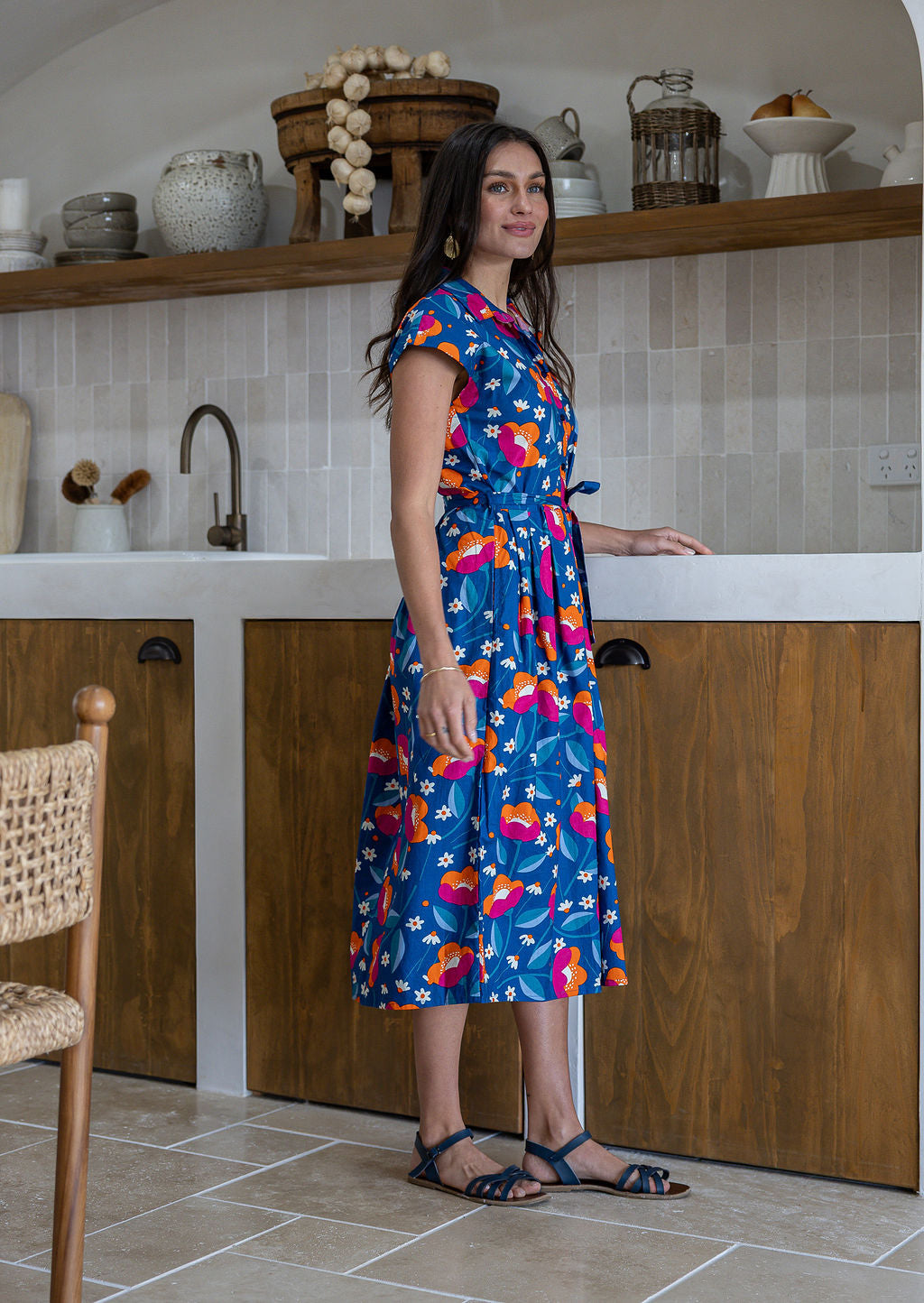 Model stands sideways near wearing a mid length, shirt style floral print cotton dress with navy based floral print