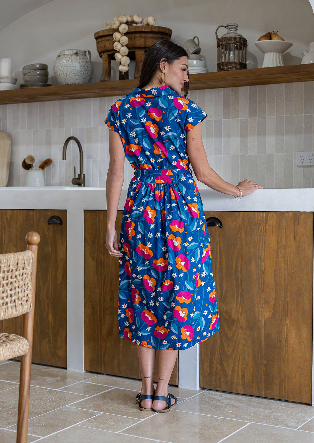 Model stands backwards near wearing a mid length, shirt style floral print cotton dress with navy based floral print