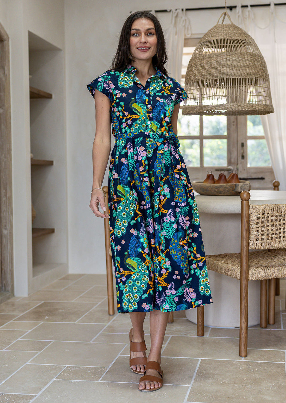 A woman modelling a cap-sleeve cotton midi dress with collar and buttoned bodice, in a vibrant multicolour floral and peacock print