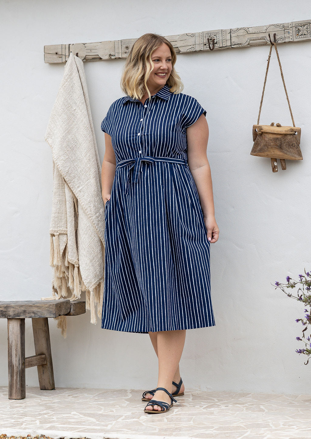 A woman wearing a navy white vertically striped midi 100% cotton dress with one hand in pocket