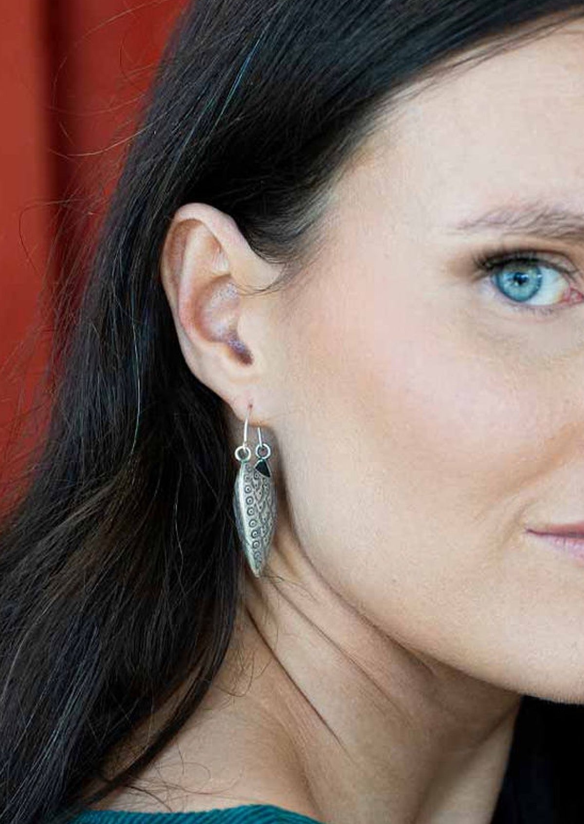Close-up of a woman wearing Hill Tribe Silver earrings with a red background