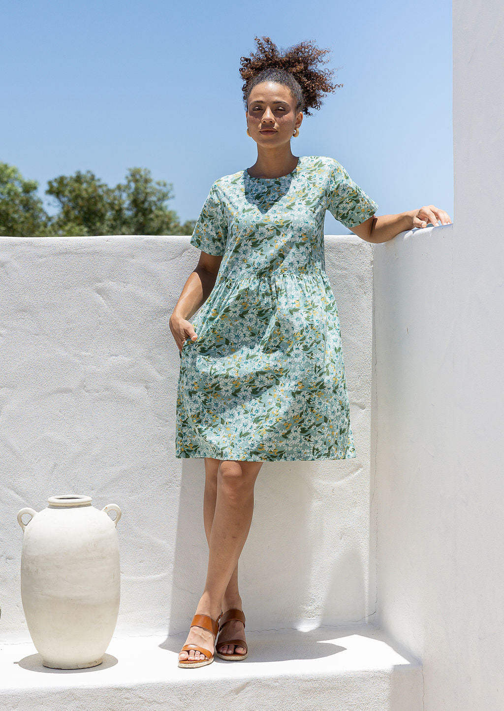 Woman wearing a 100% cotton relaxed fit dress with round neckline and short sleeves in sage green based floral print.
