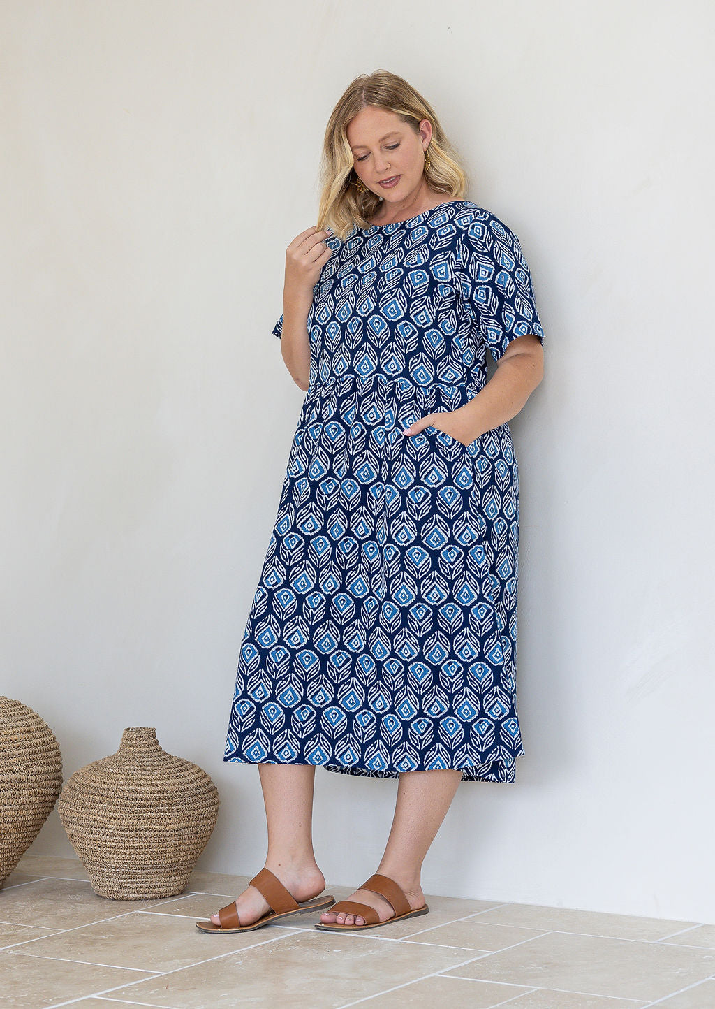 Model poses in relaxed fit cotton midi length dress with short sleeves and high round neckline with one hand in pocket
