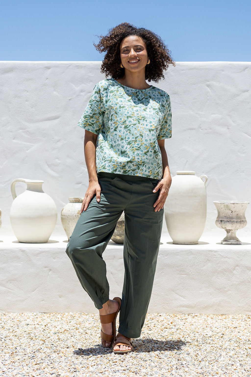 Woman in sage green based floral cotton top with short sleeves, round neckline and plain green pants.