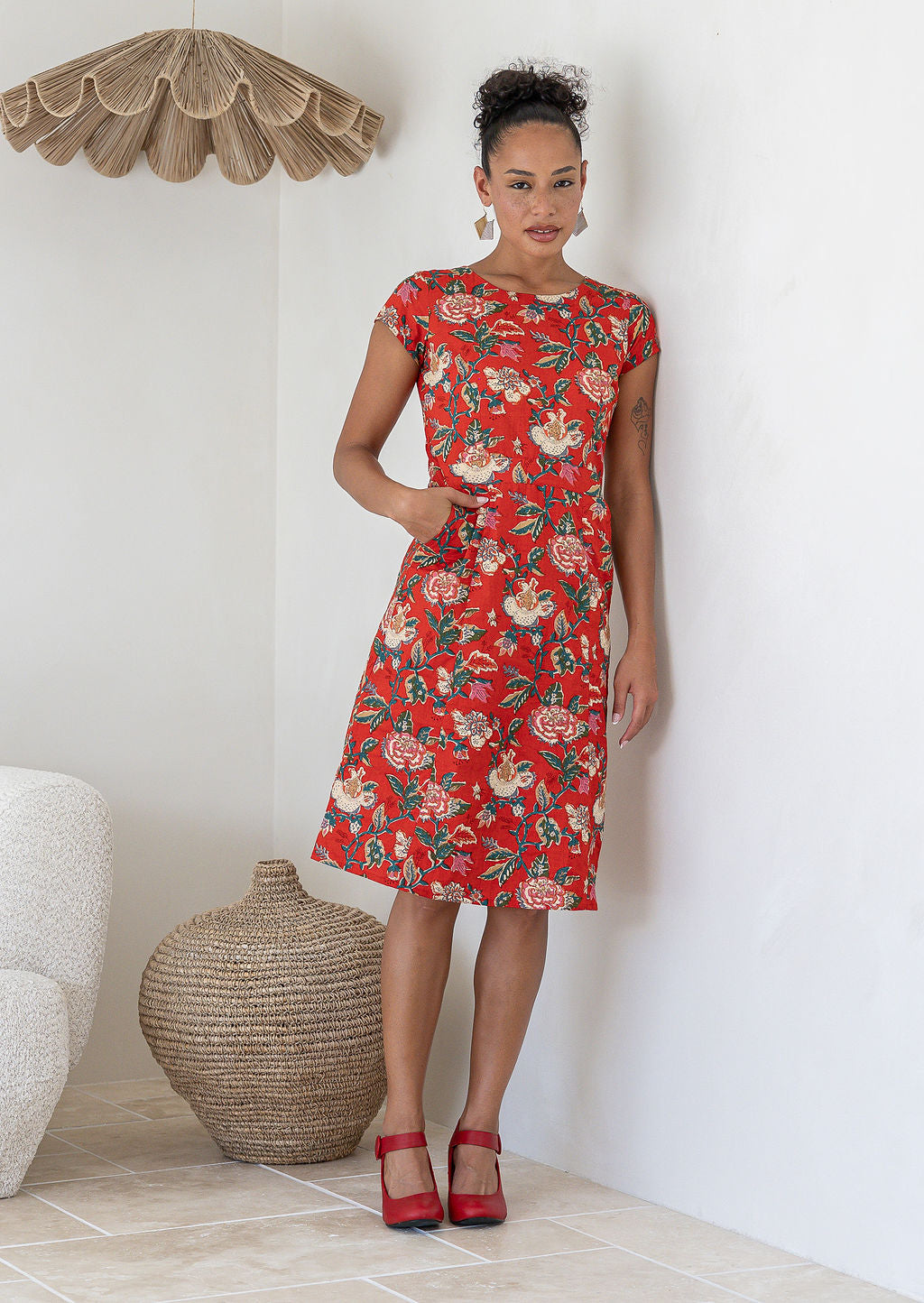 Woman wearing a cap sleeved 100% cotton floral print dress with red backdrop accented by elegant multicoloured floral vines.