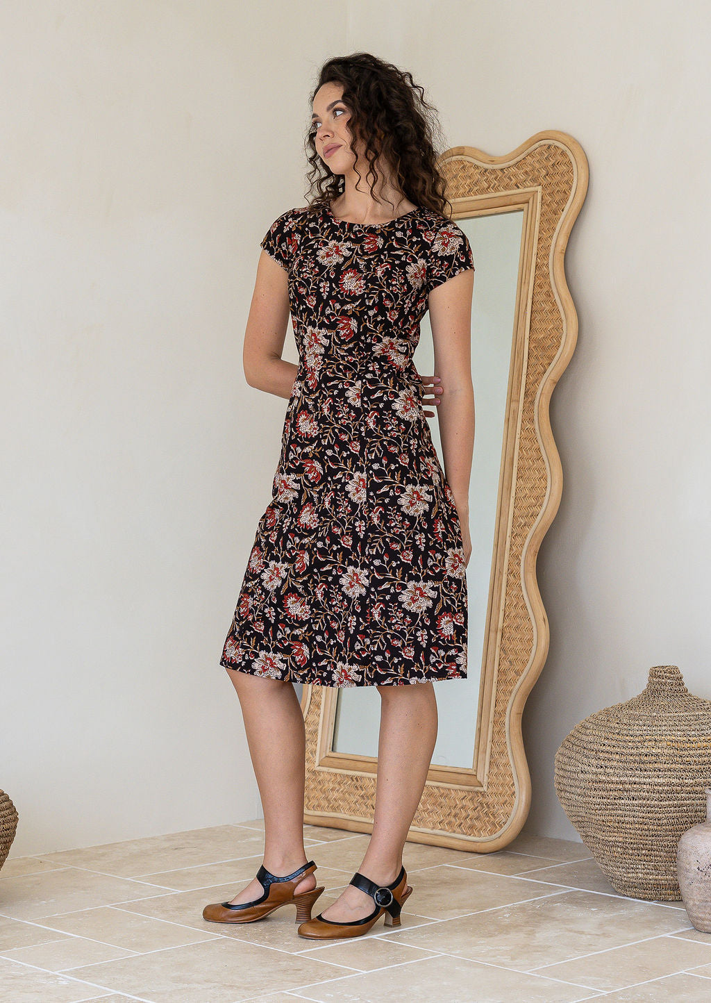 Model posing in a black floral print shirt style 100% cotton dress with cap sleeves