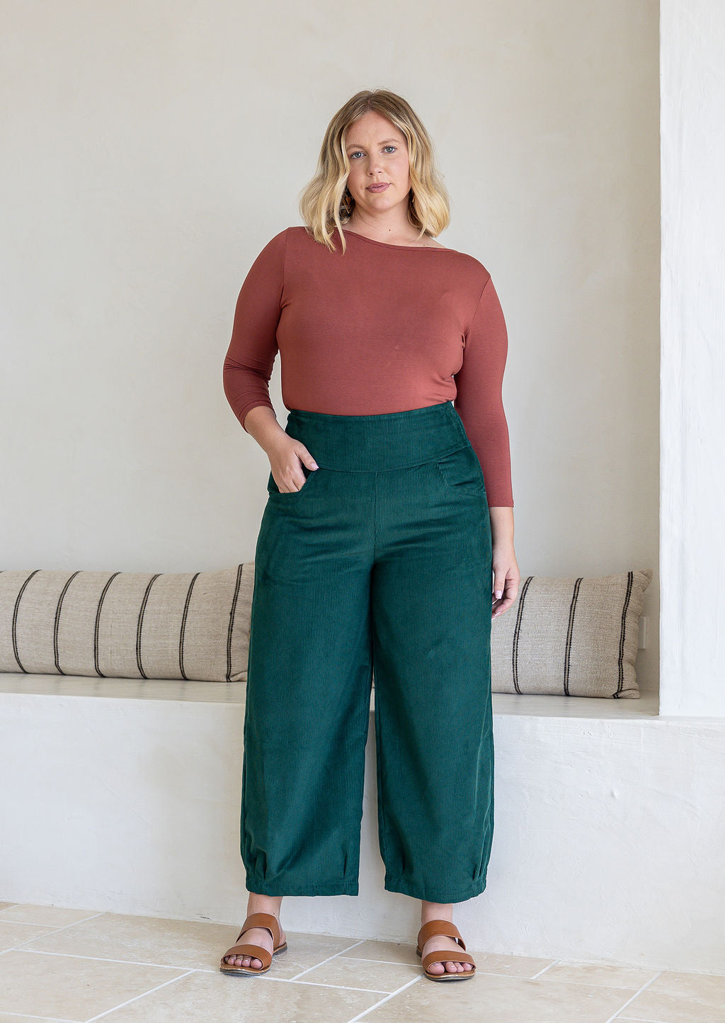 Woman posing in cotton corduroy wide-leg dark green pants with wide flat waistband, with one hand in pocket