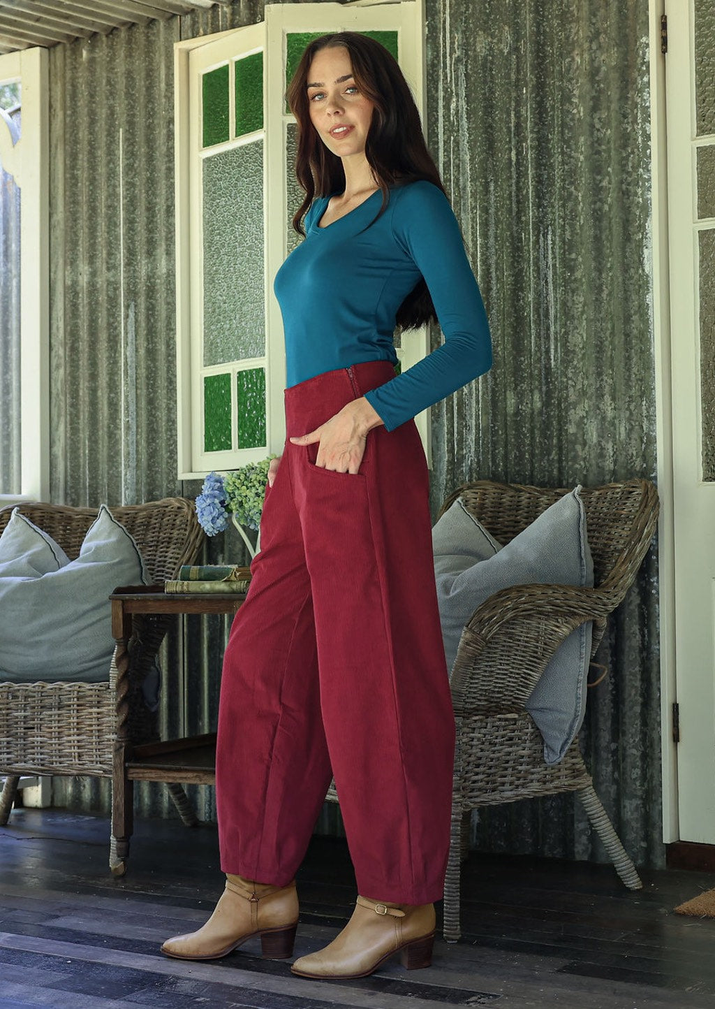 Woman in a red corduroy pants standing in a room with wicker furniture and green walls.