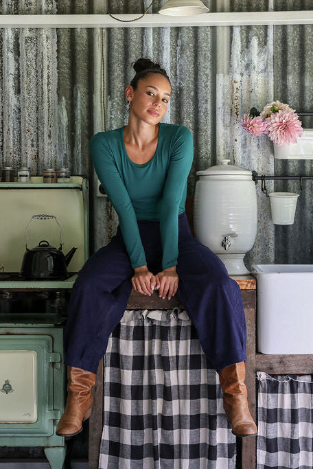 Woman sitting on a stool in a rustic outdoor setting with corrugated metal walls.