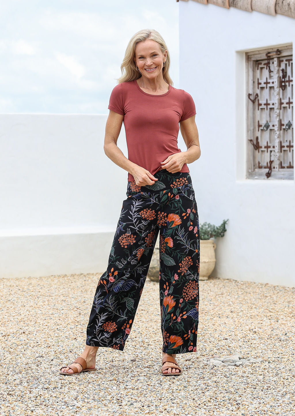 Woman wearing cotton wide leg pants in black based botanical print, paired with terracotta basic rayon top