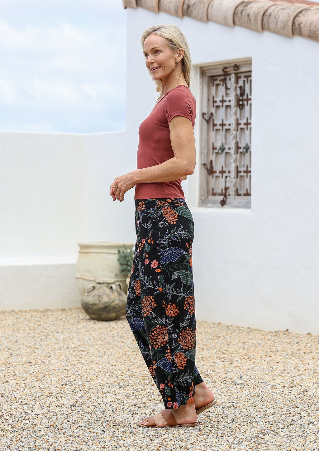 Model standing sideways wears 100% cotton wide leg pants with side zipper, pockets and small pleats at ankles.