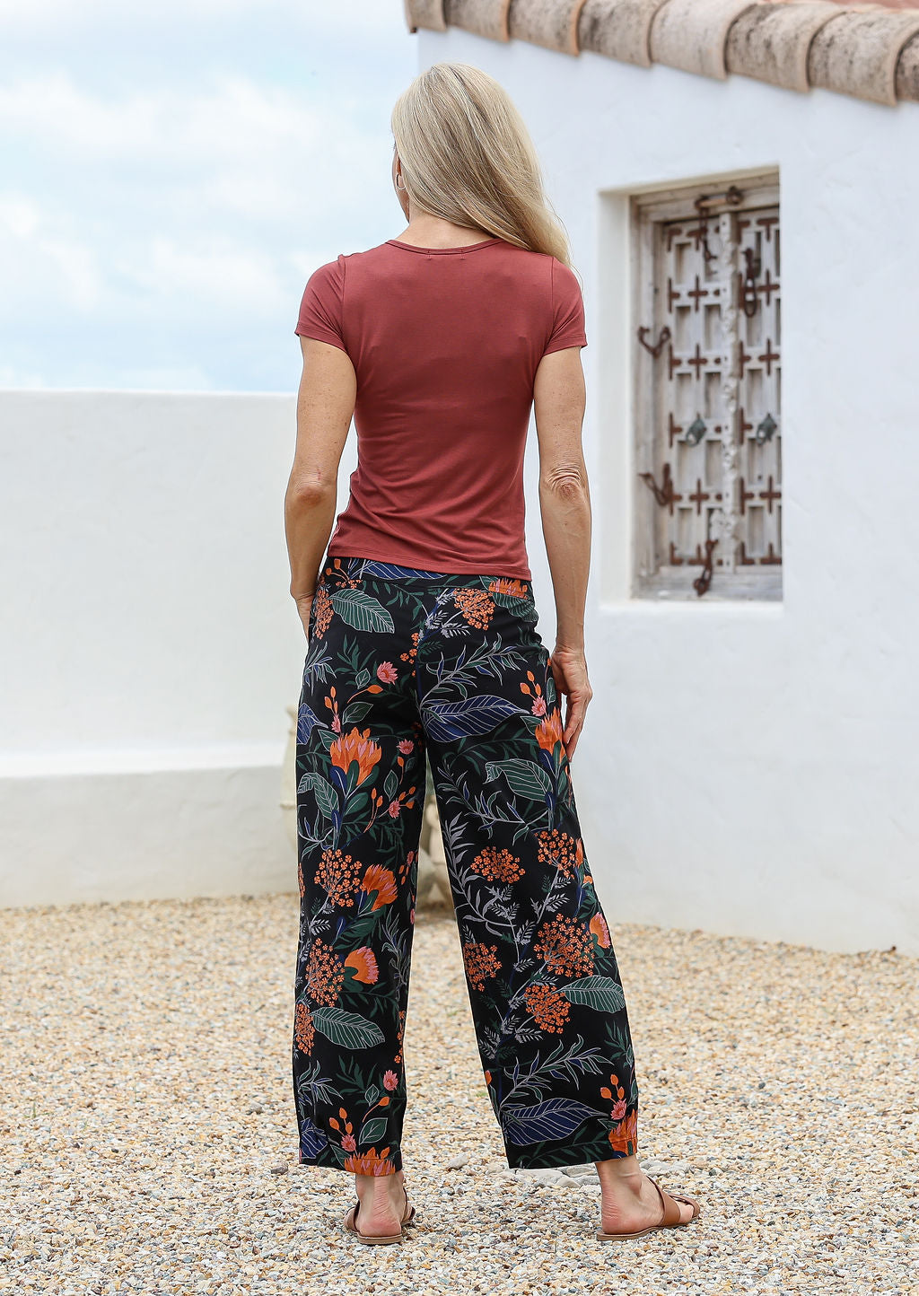 Model standing in a back pose wears wide leg cotton pants with pockets and side zipper in black based botanical queen protea print