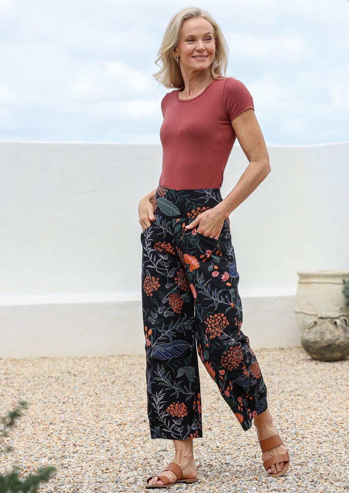 Woman wearing a basic rustt top and black native floral, wide-leg cotton pants, standing outdoors with hands in pockets