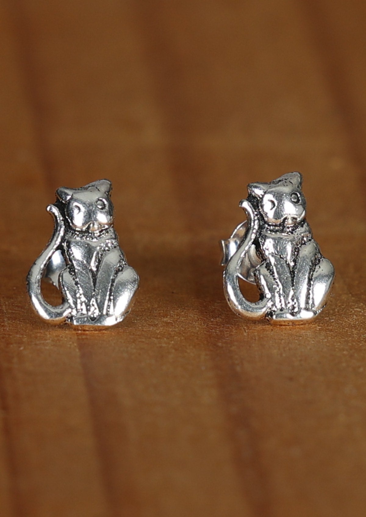 Close-up image of Happy Cat silver cat-shaped stud earrings sitting on a wood surface.