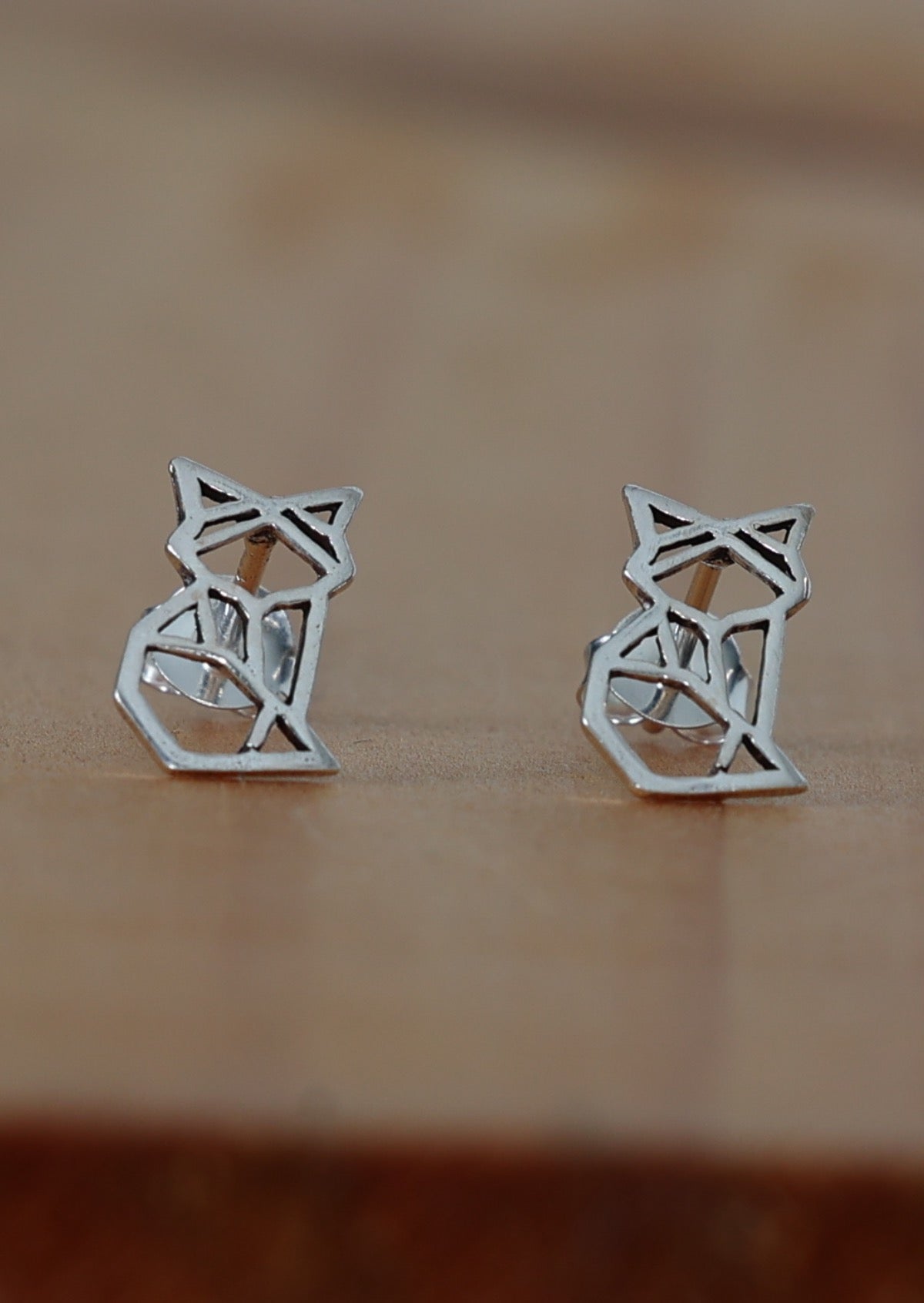 A pair of silver geometric fox stud earrings placed on a wooden surface.
