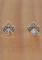 A pair of sterling silver boho heart stud earrings featuring a tribal-inspired shape within a heart outline, displayed on a wooden surface.