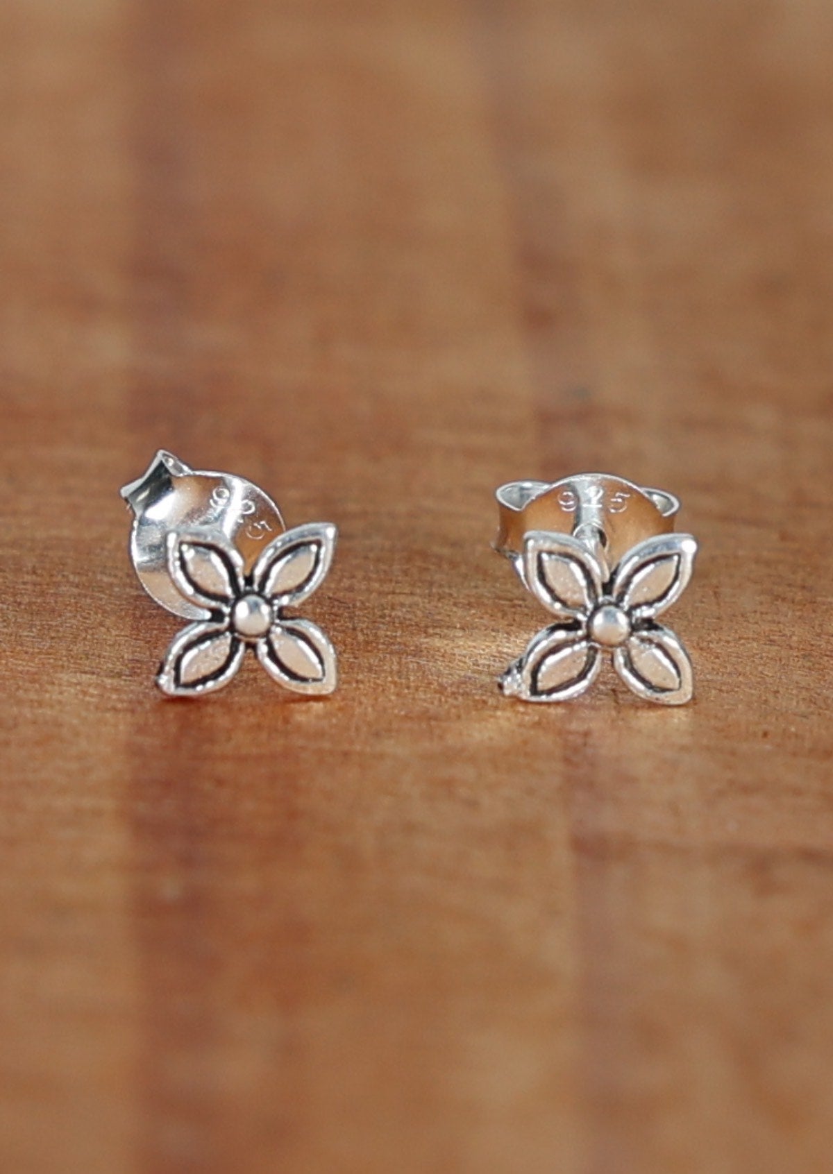 A pair of sterling silver stud with a 4 curved petal design, displayed on a wooden surface