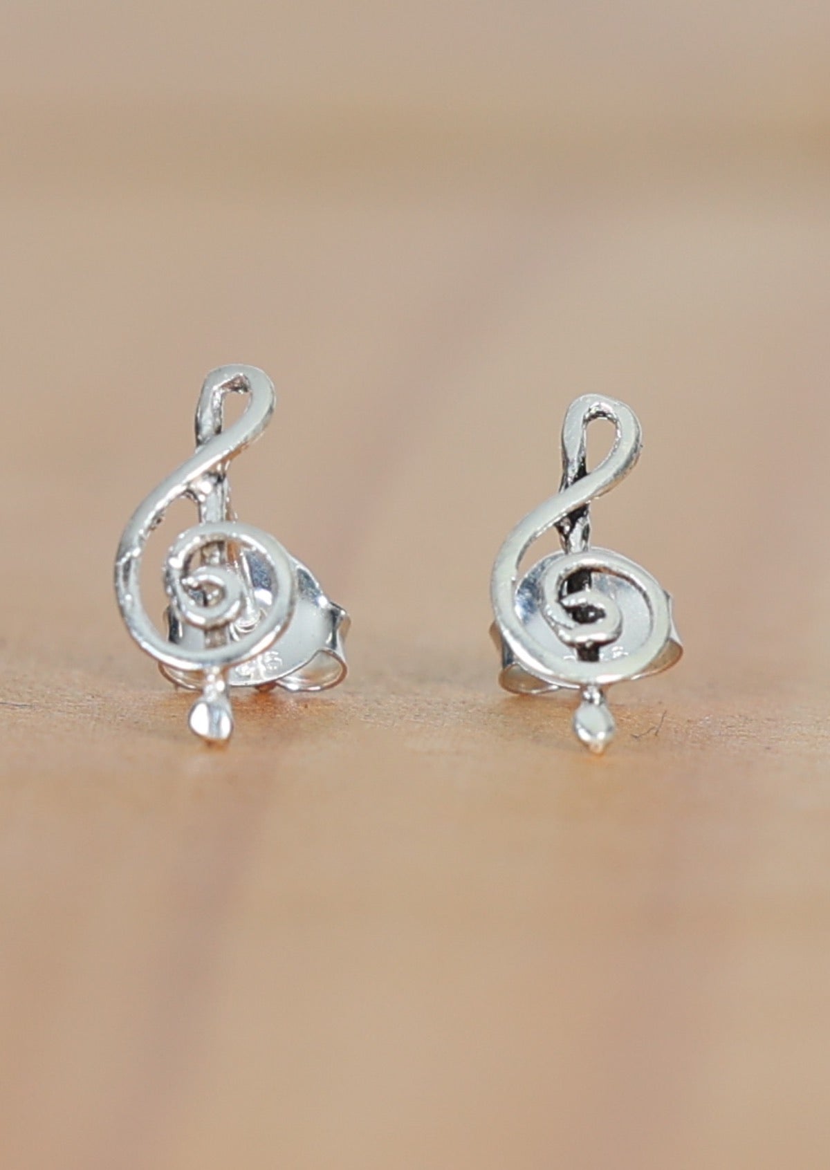 A pair of sterling silver stud earrings with a curved treble clef design displayed against a wooden background