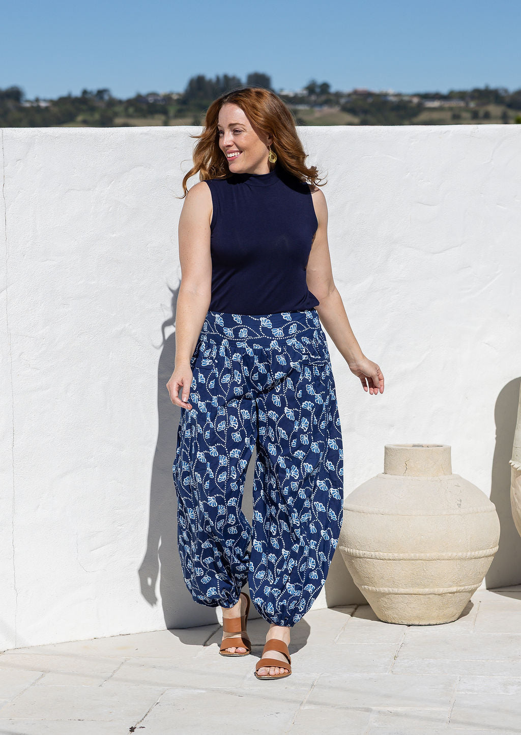 Woman wearing a basic top and blue based floral pants with wide elastic waist and ankles.