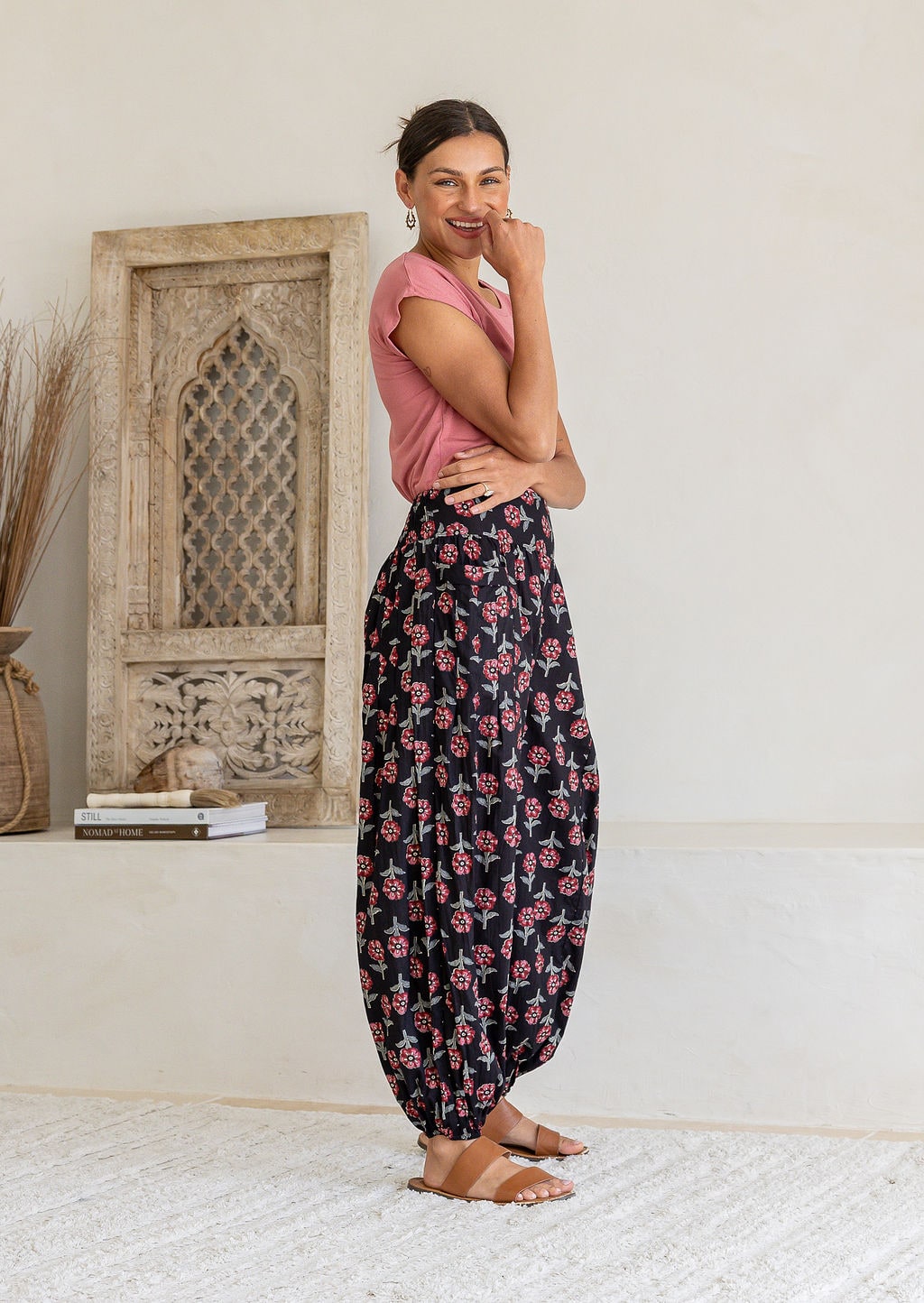 Woman stands sideways wearing a basic top and blue based floral pants with wide elastic waist and ankles.