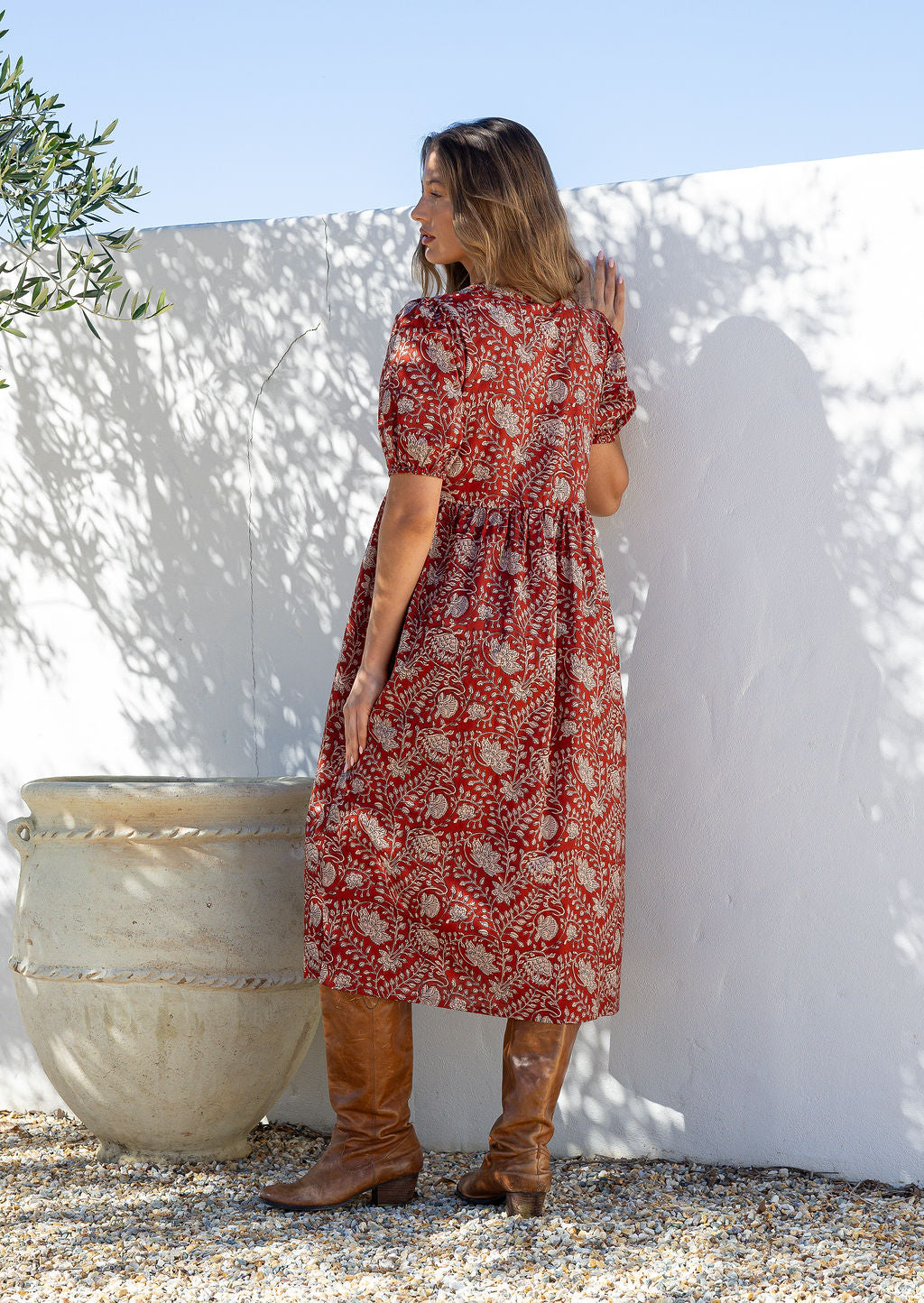 Woman standing backwards in a red floral cotton button through dress with elbow length puffy sleeves and a V-neckline.