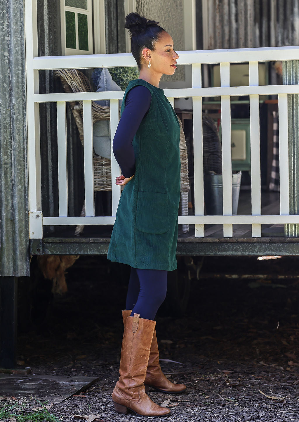 Woman in a green dress and brown boots standing on a rustic porch.