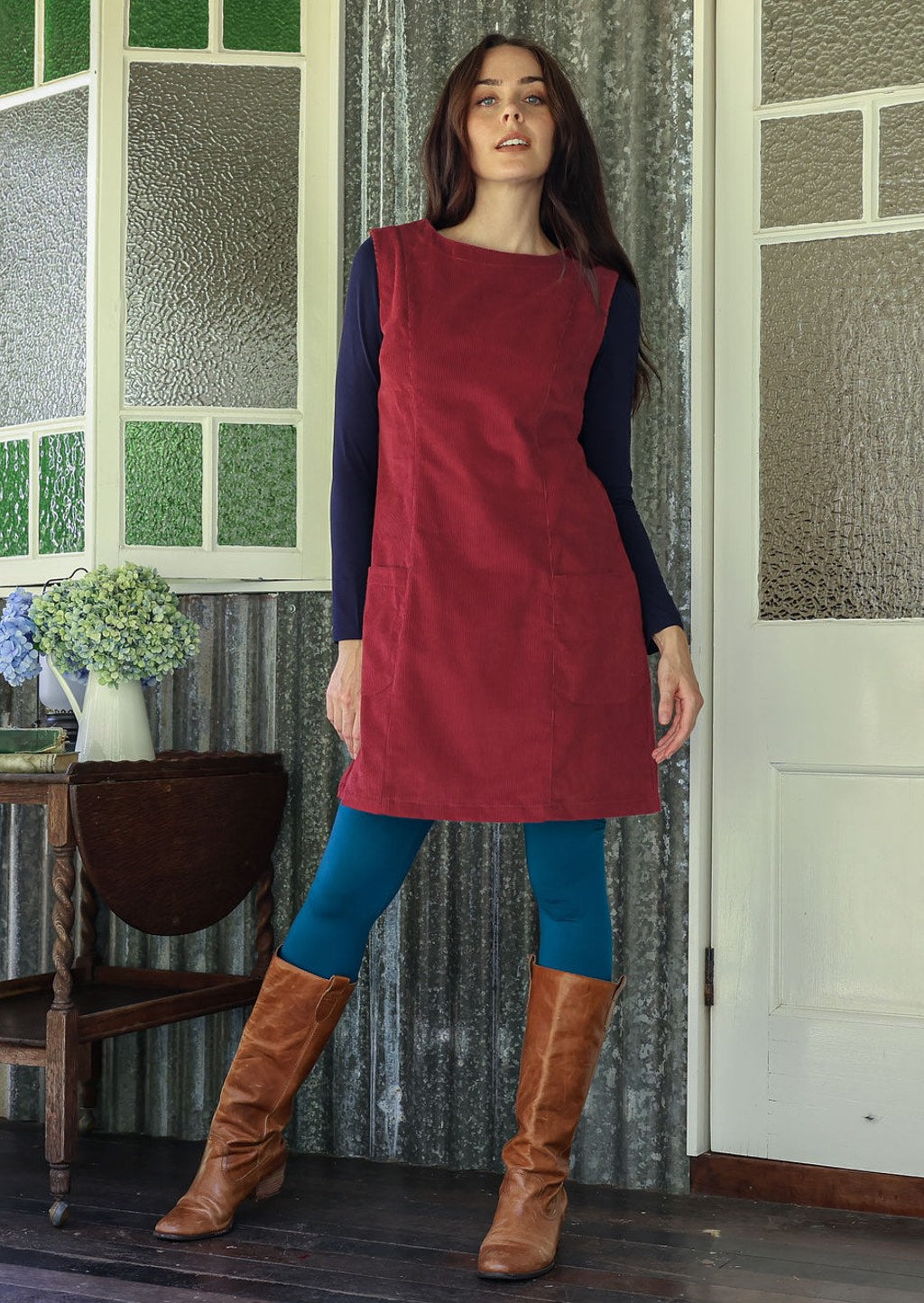 Woman wearing a red dress and blue leggings standing in a room with patterned wallpaper.