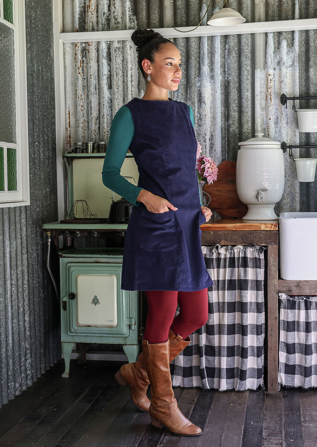 Woman in a blue dress and red leggings standing in a rustic kitchen.