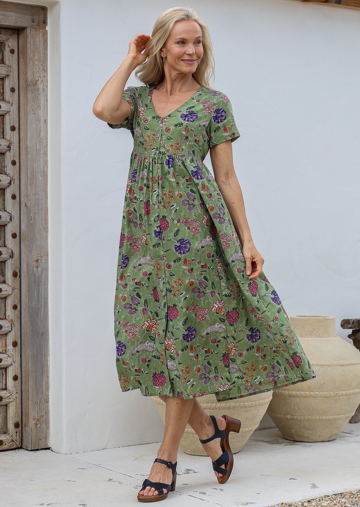 Woman wears 100% cotton button through relaxed fit dress with short sleeves and V-neckline in folk art style floral print on a moss green base.