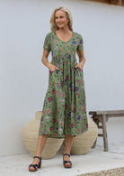 Woman standing with both the hands in pockets wearing a relaxed fit midi length cotton dress with empire waistline and gathered design.