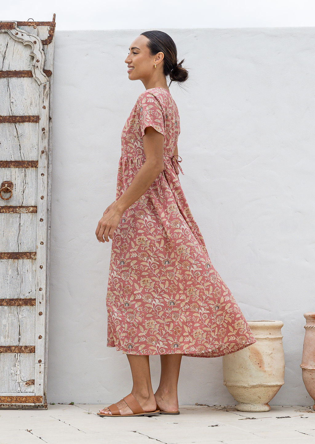 Woman stands sideways wearing a 100% cotton dress with short sleeves, pockets, and a drawstring tie at the back.