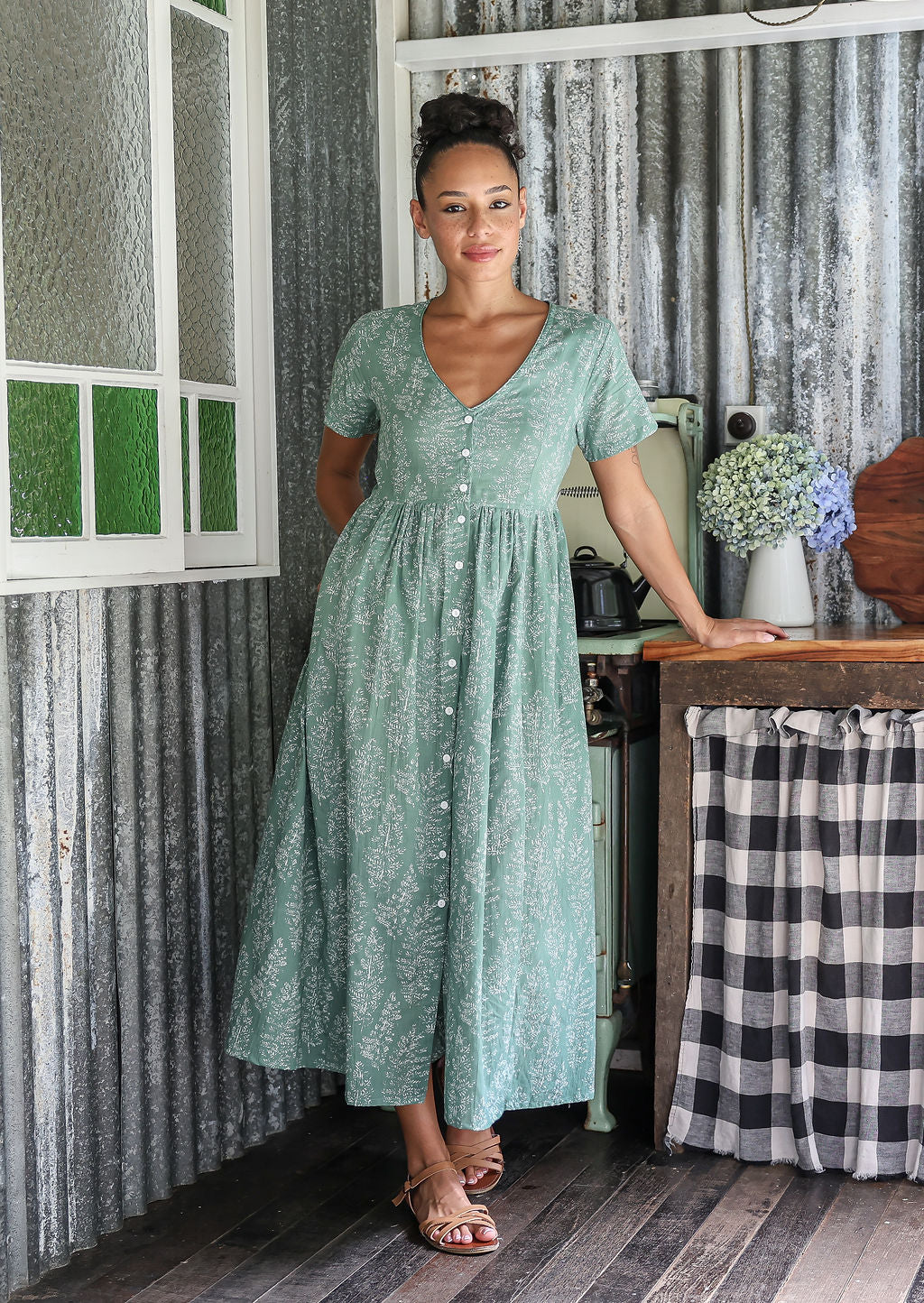 Woman standing in a 100% cotton floral print dress with a V-neckline, short sleeves, pockets, and buttons through to the knee.