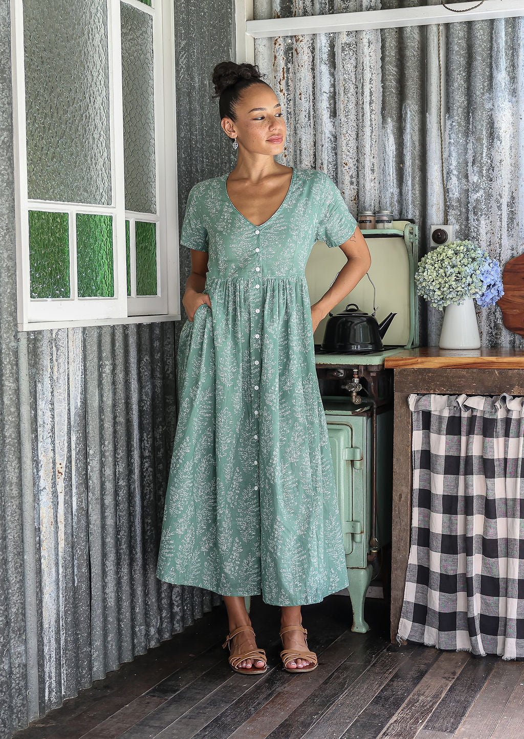 Woman wearing a relaxed fit, button through cotton dress in sage green base floral print with V neckline.