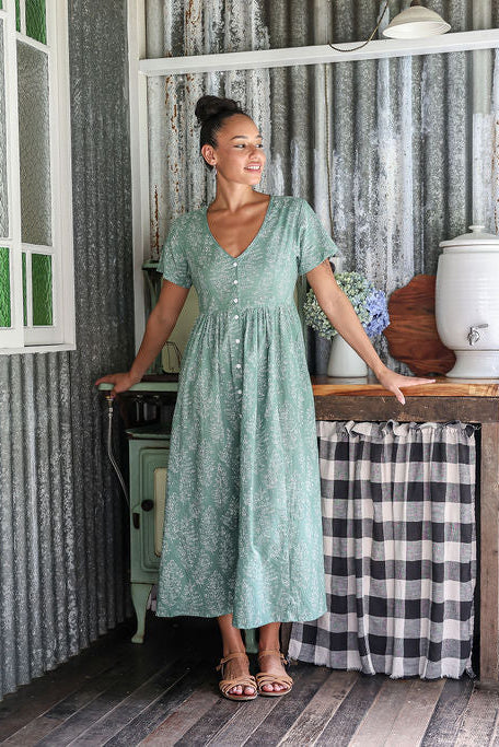 Woman in a green dress standing in a rustic bathroom with wooden fixtures and checkered towels.