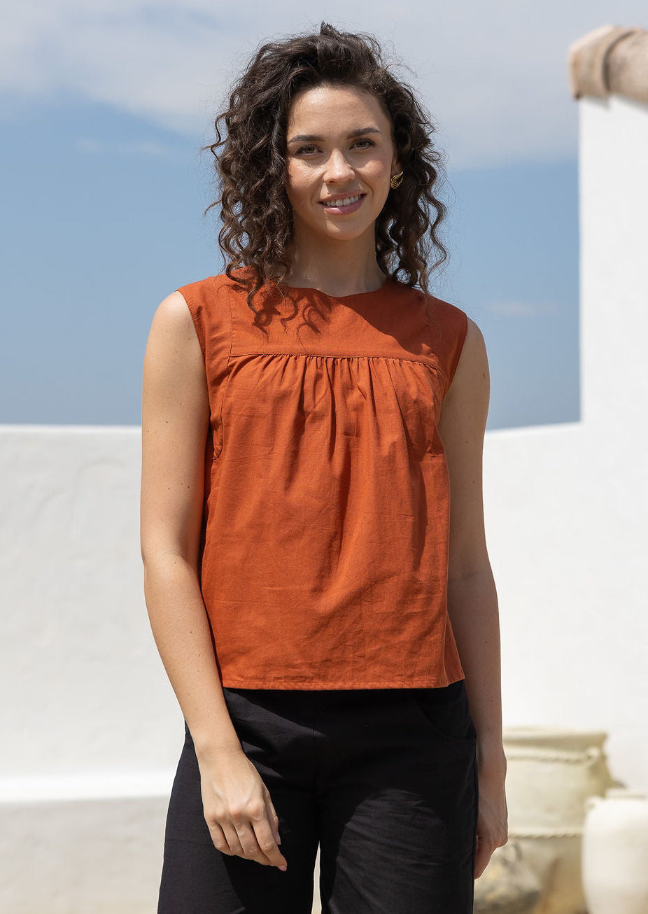 Woman wears rust tone cotton sleeveless top with small gathers across the bust