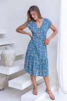 woman standing in blue based floral print non-stretch rayon dress with V-neckline and small gathers under bust