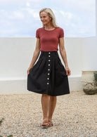 Woman standing outdoors wears 100% cotton tailored knee length skirt with button up front, box pleats and pockets