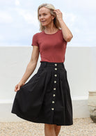 Woman wearing terracotta basic top paired with 100% cotton knee length tailored A-line skirt with box pleats, buttoned front and belt loops
