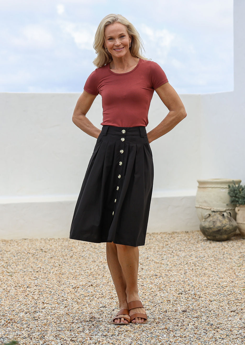 Woman posing in knee length black cotton button-up skirt with belt loops, pockets and box pleats