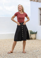 Woman wearing terracotta basic top and black cotton pleated skirt with button through front, pockets and belt loops.