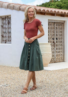 Model posing in a 100% cotton pleated A-line skirt in jungle green with belt loops, box pleats and pockets
