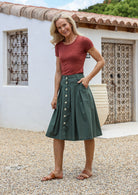 Woman wearing a basic rayon top and knee length, A-line cotton skirt in jungle green with button up front, pockets and belt loops