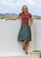 Woman wearing tailored A-line cotton skirt in jungle green with button up front, pockets and belt loops