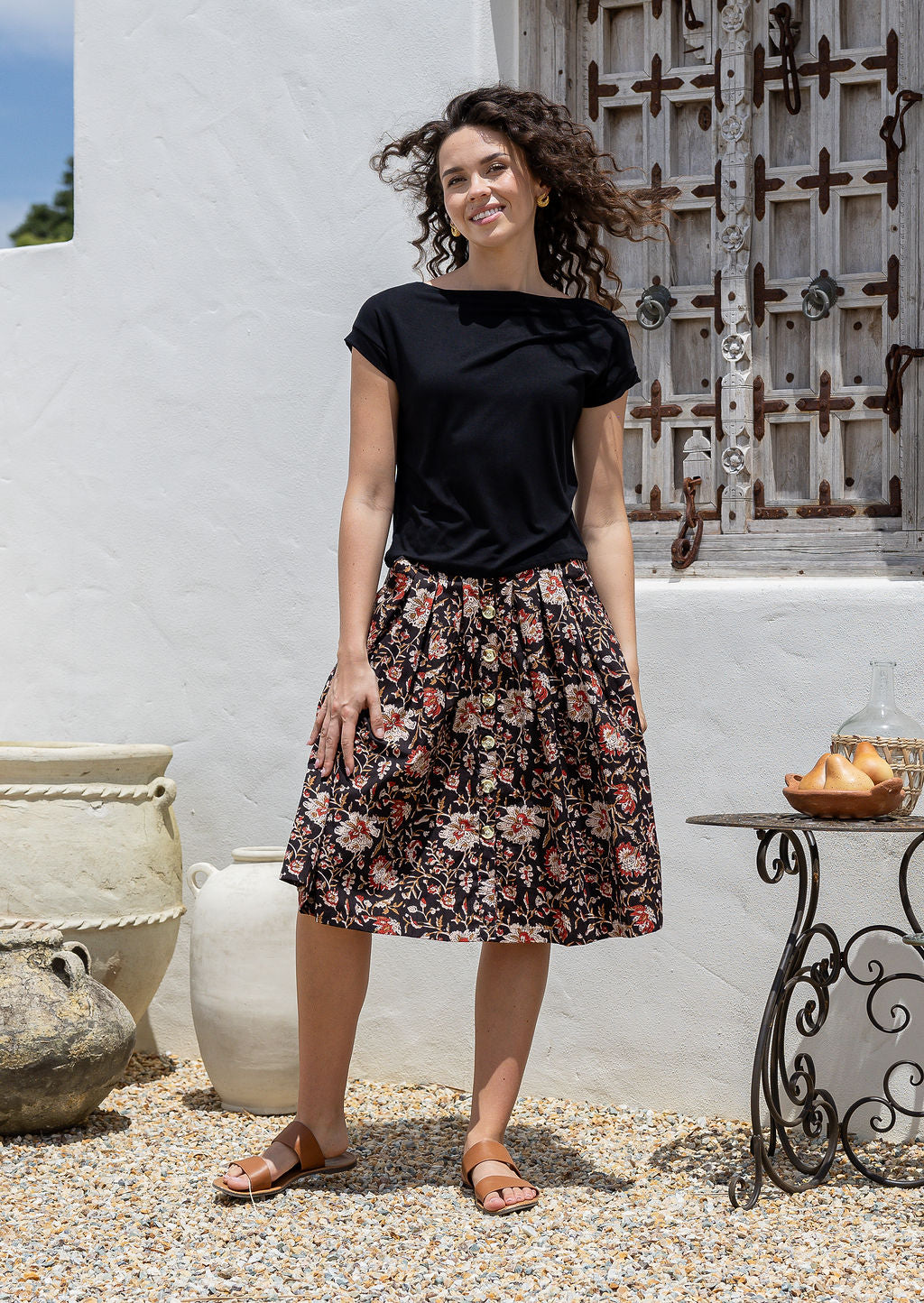 Woman wearing a basic black top and knee length button through cotton skirt with box pleats belt loops and pockets