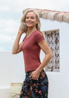 Woman wearing a terracotta shirt and floral pants standing outdoors with a house in the background